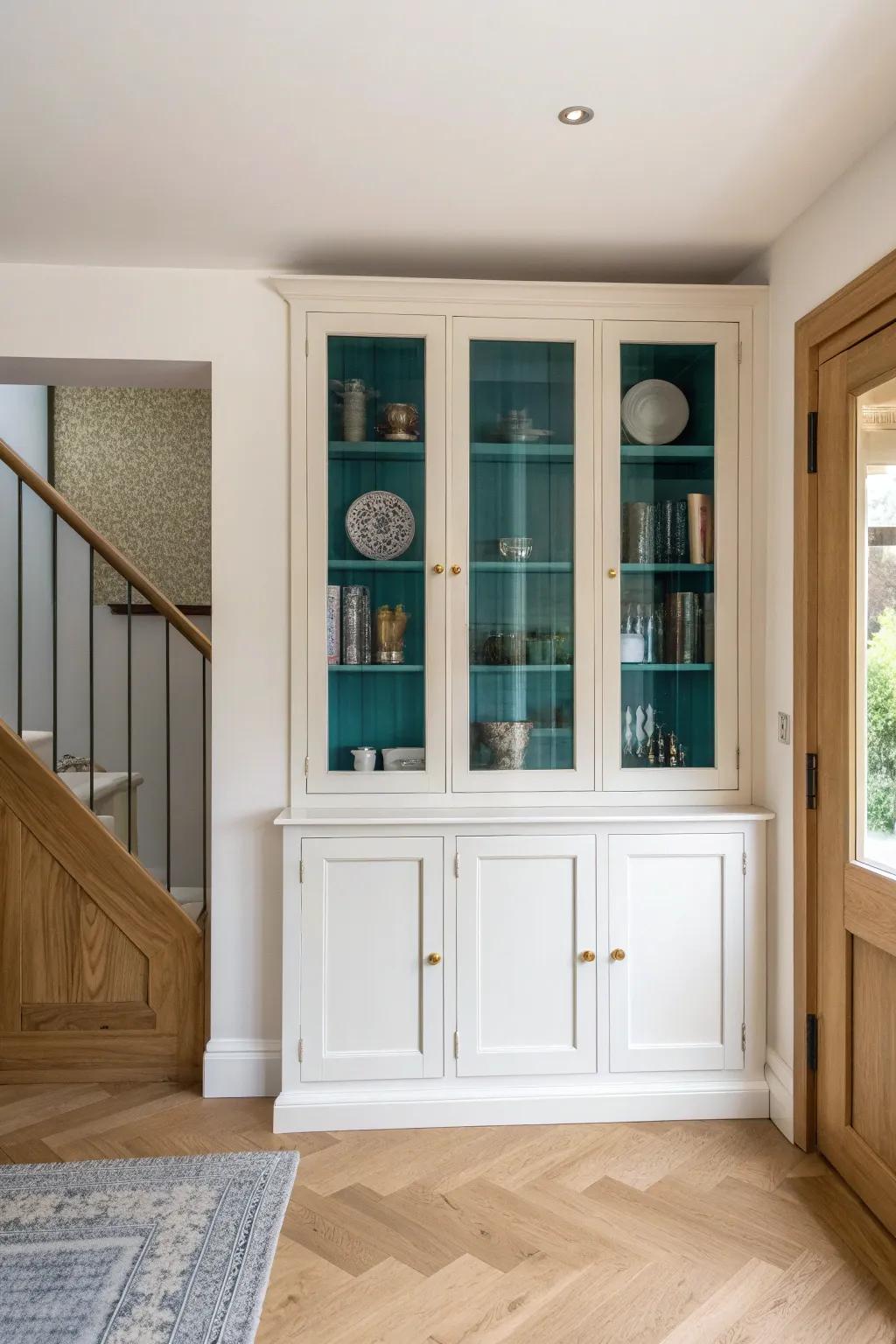 A seamless alcove-fit china cabinet—scribed to the wall, with bold teal backing and warm oak.