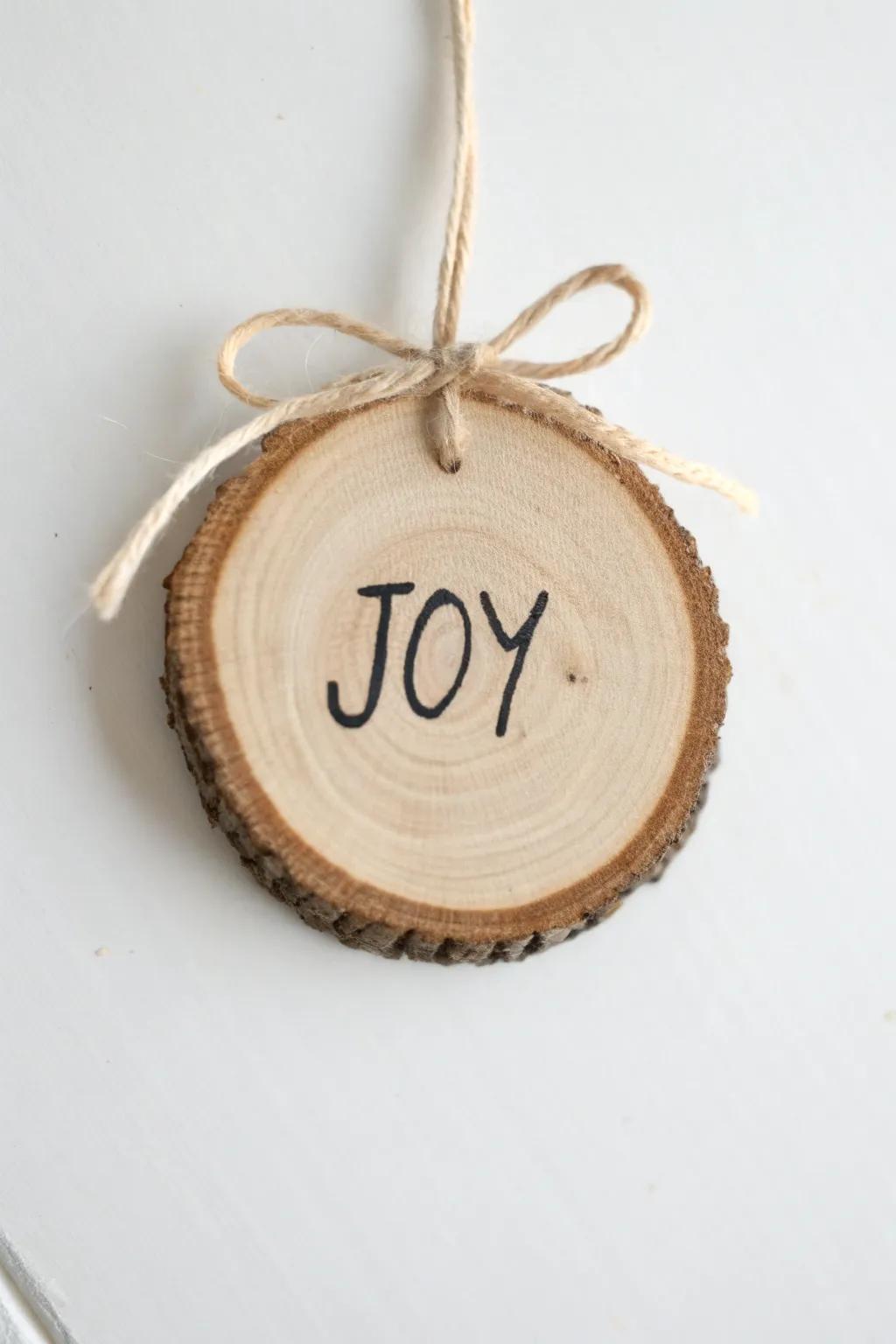Handwritten “JOY” on a wood slice ornament—simple twine, soft bow, and natural grain beauty.